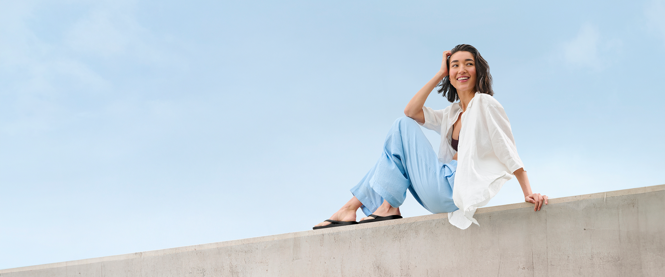 Woman on ledge wearing Black Archies Flip Flops 