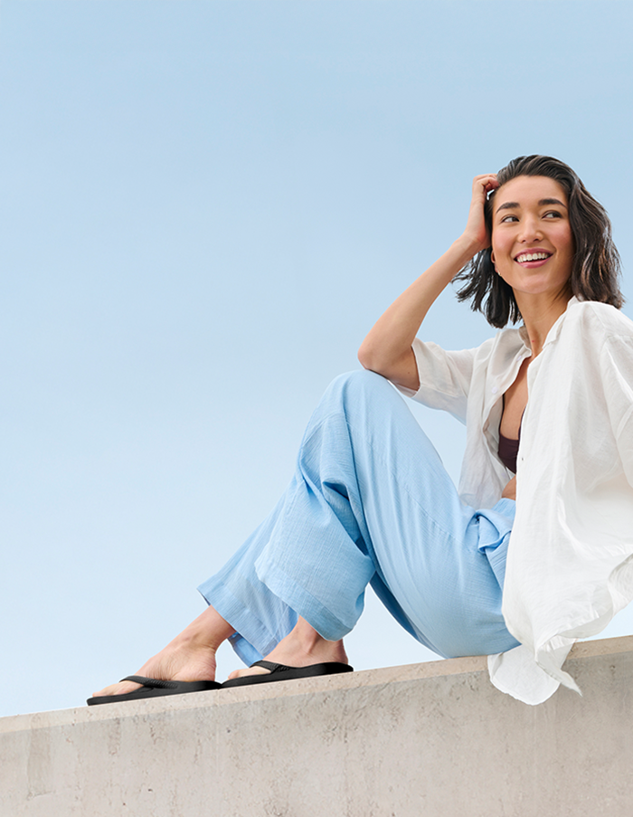 Woman on ledge wearing Black Archies Flip Flops 
